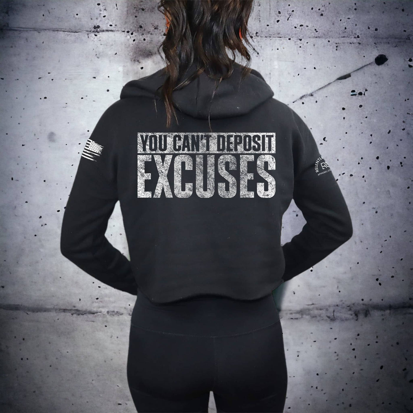 Person wearing a black hoodie with motivational text on the back against a textured wall.