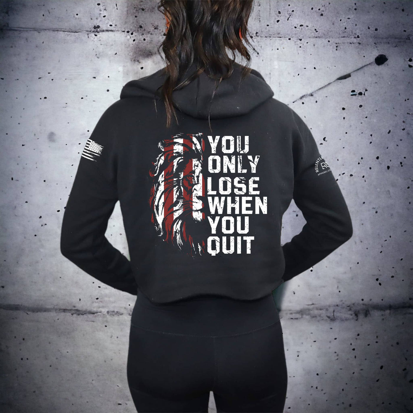 Person wearing a black hoodie with motivational quote on the back against a gray concrete wall.