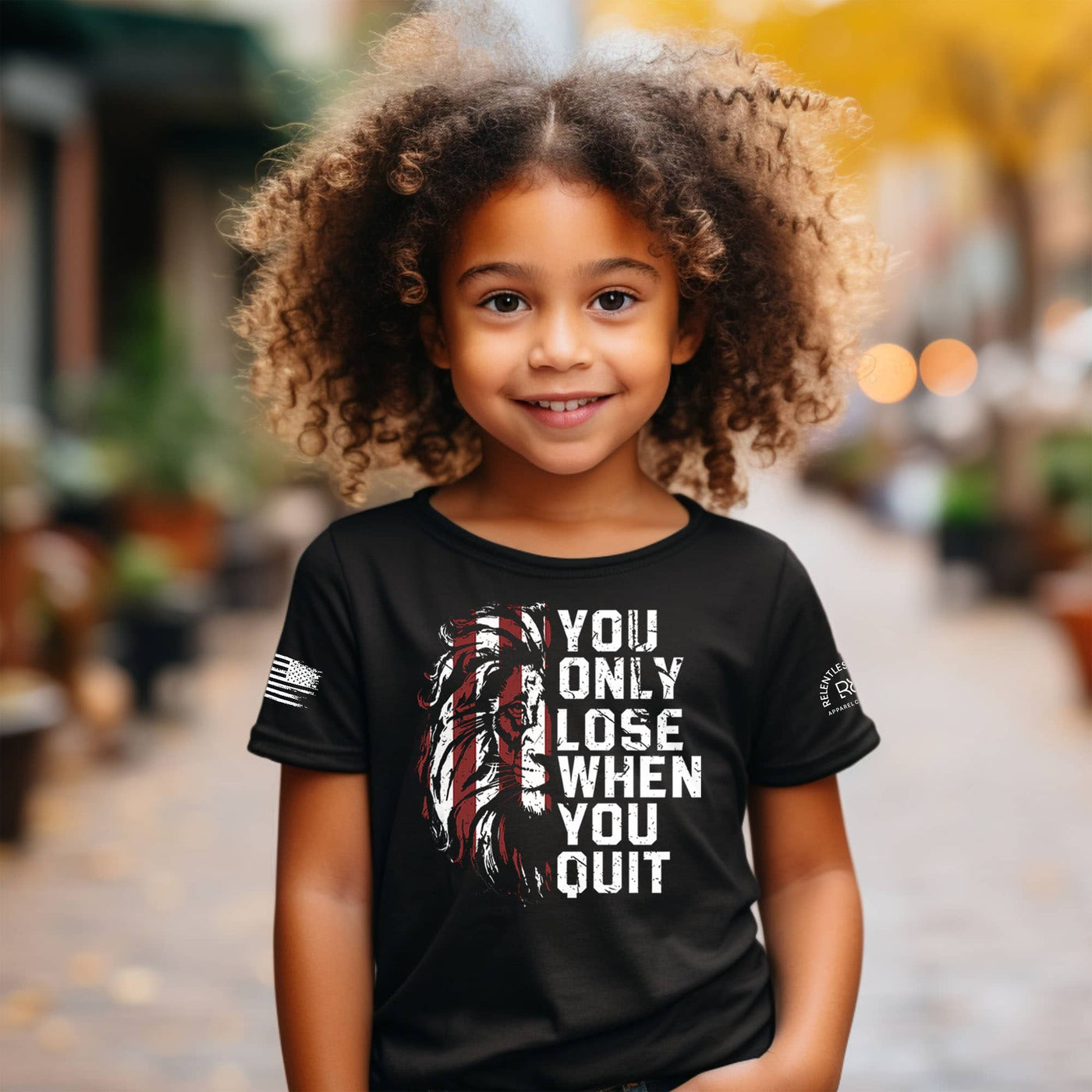 Child wearing a black t-shirt with a motivational quote and graphic design, standing outdoors.